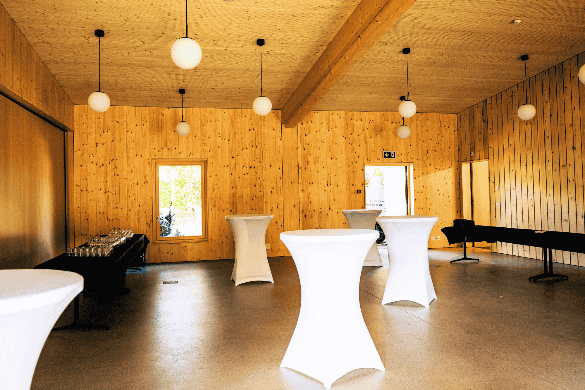 Intérieur du Pavillon du Théâtre du Jorat montrant des tables hautes nappées de blanc et des tables de buffet.