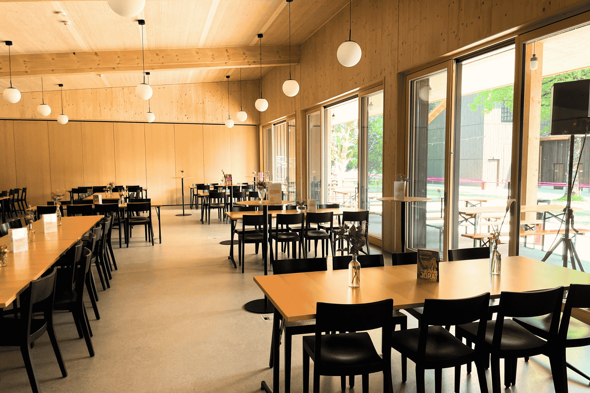 Intérieur du Pavillon du Théâtre du Jorat avec tables, chaises, luminaires et petite décoration.