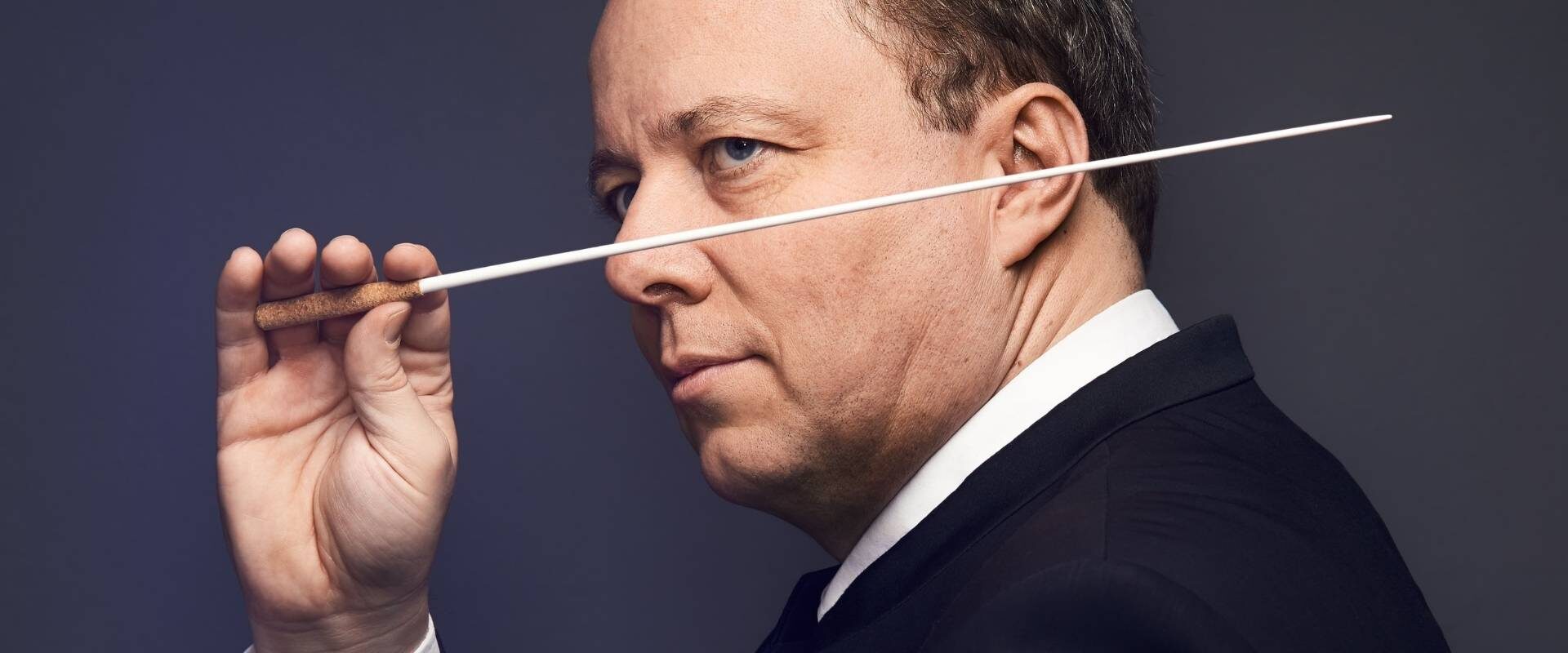 Le chef d'orchestre Nicolas Chalvin pose avec sa baguette de direction qu’il brandit devant son nez.